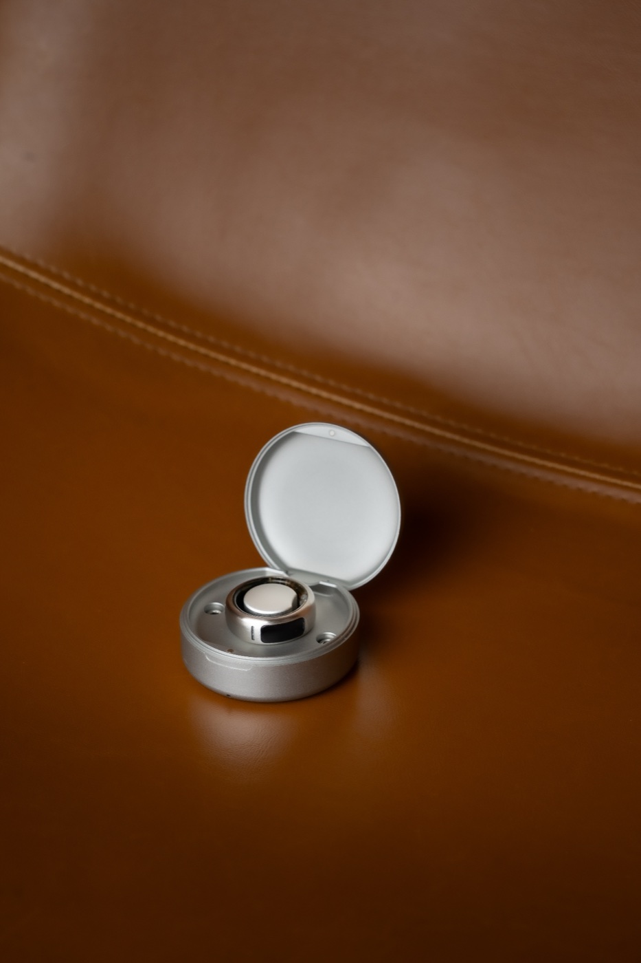 The OASIS ring and its charging case, resting on leather